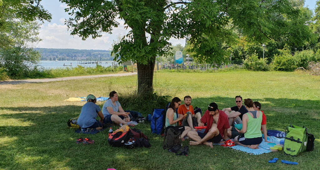 Mehrere Personen sitzen auf einer Wiese unter einem Baum.